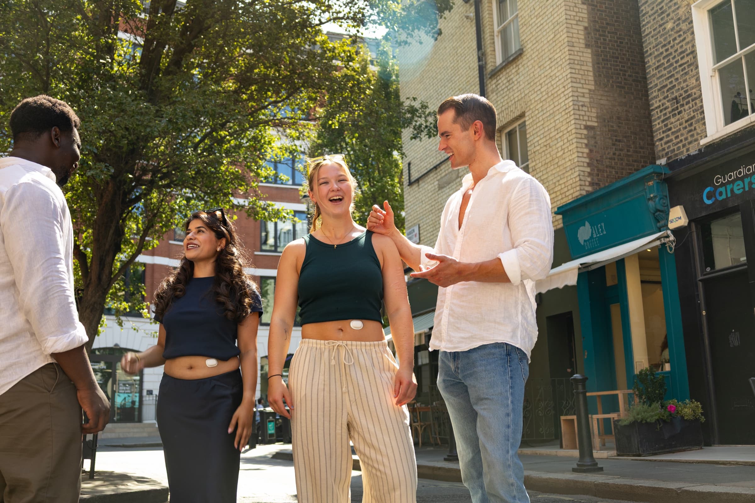 Three models laughing together on a city street, one wearing the Suna device