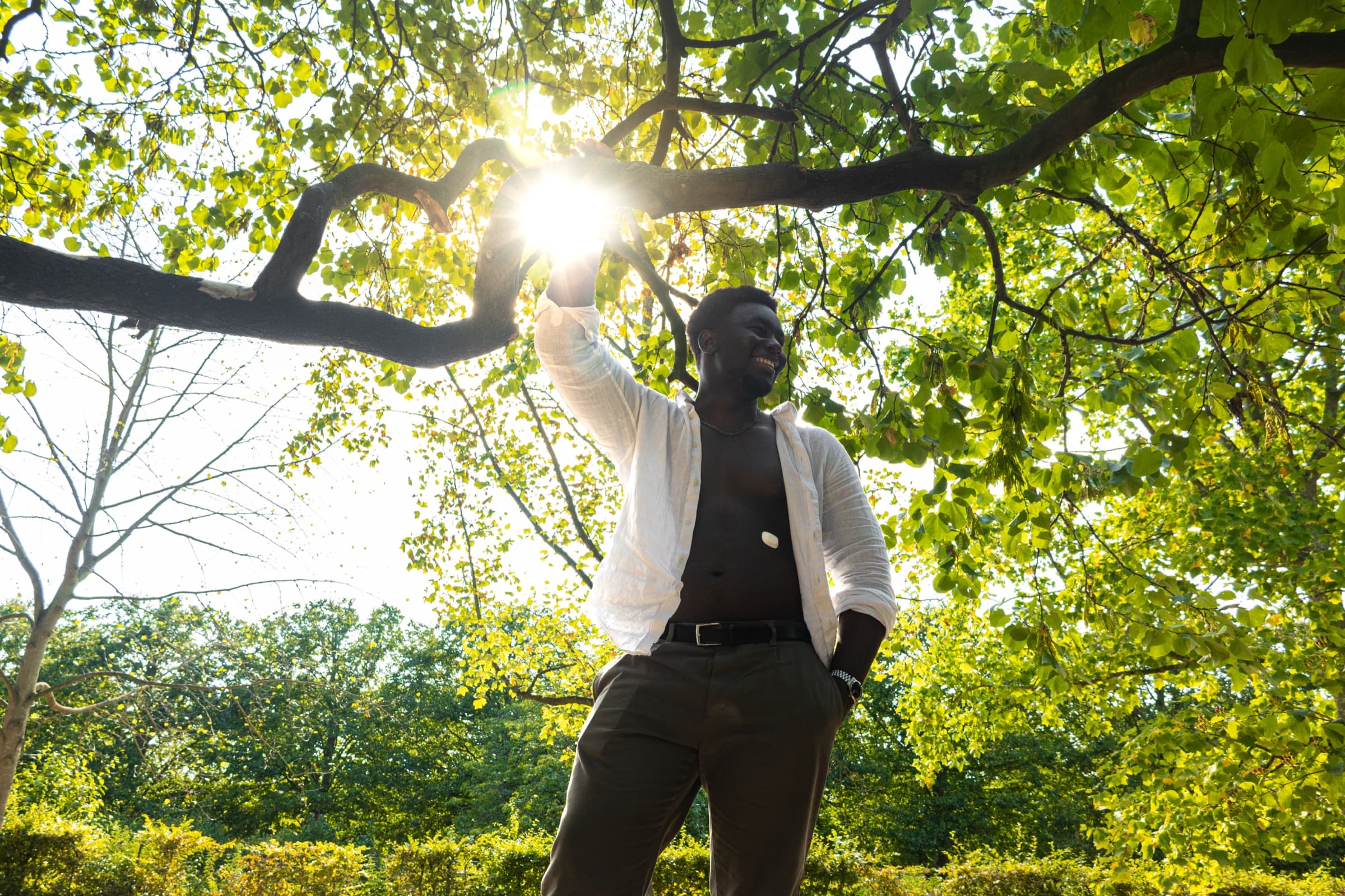A model in a white shirt under a tree in low sun, wearing the Suna device