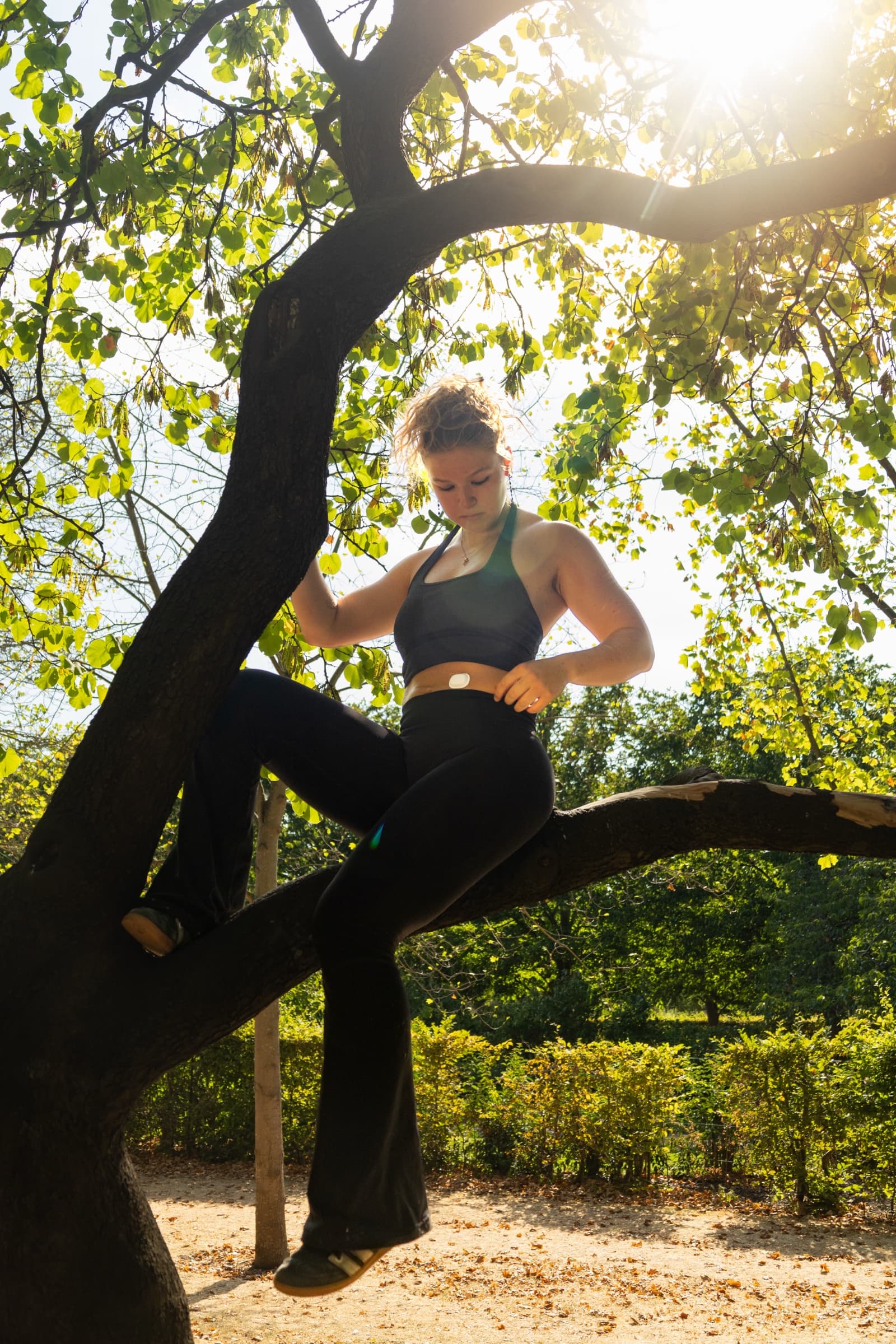 A model in black activewear climbing a tree in a park, wearing the Suna device
